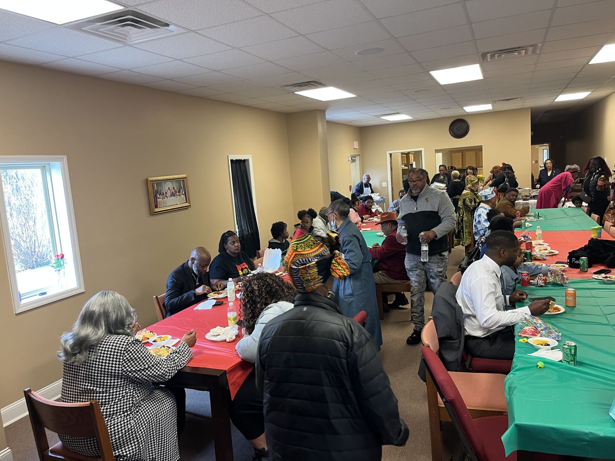 Church members sharing a meal at long red and green tables in the fellowship hall