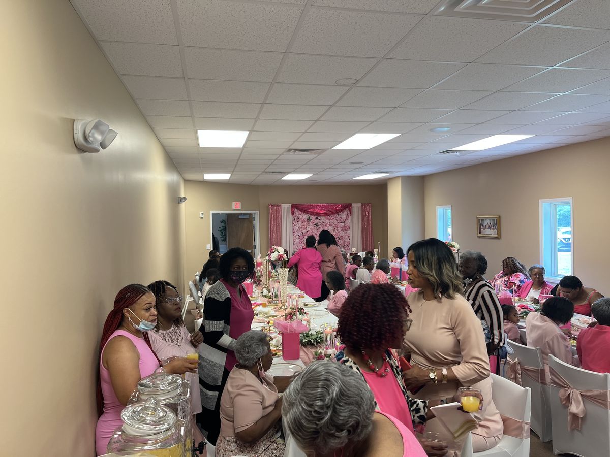 Women dressed in pink gathered around decorated tables in the fellowship hall